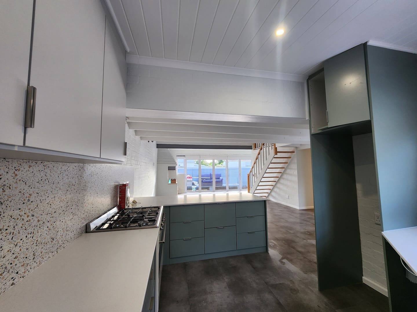 Kitchen with deep teal cabinetry, terrazzo splashback and a staircase beyond